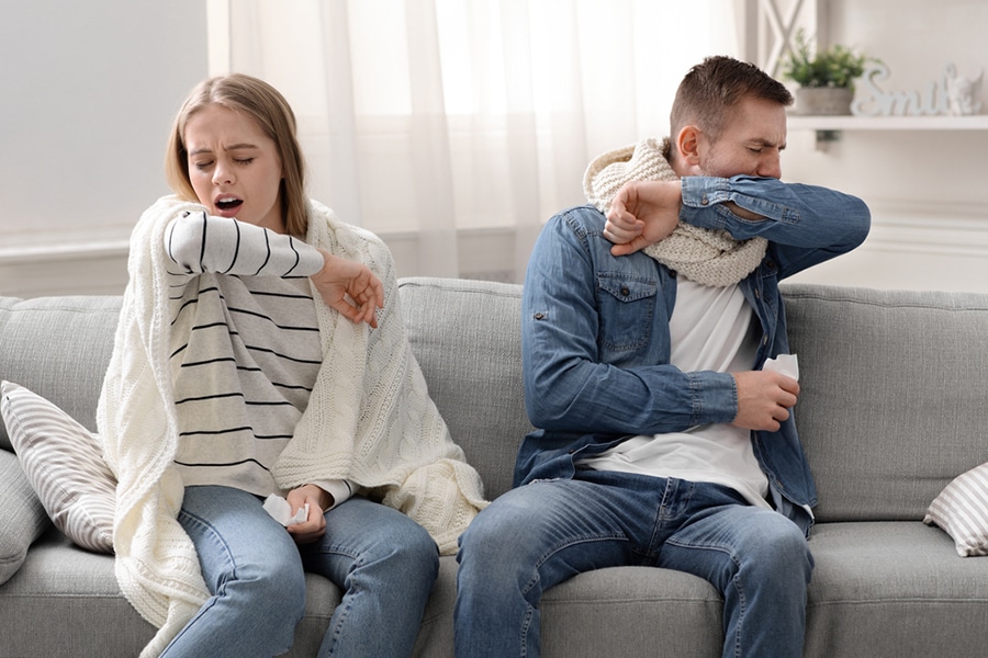 man and woman coughing into their elbows