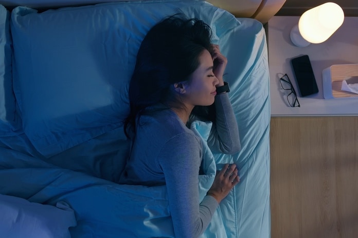 A woman is turned over on her side as she sleeps in a bed. There is an alarm clock on a nightstand next to the bed.
